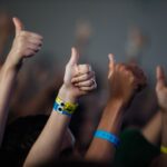 A group of diverse hands giving a thumbs up with colorful wristbands, showing unity and support.
