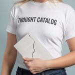 A woman wearing a white t-shirt holds a book with a cracked cover.