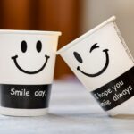 Two paper cups featuring smiley faces and positive text, encouraging happiness.