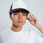 Young man wearing a white cap and casual white shirt, posing in a studio setting.